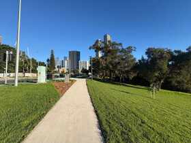 Wide concrete streetscape path with new garden bed against a city skyline